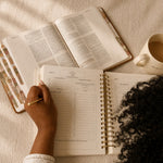 Hands writing in The Anchored Planner beside an open Bible