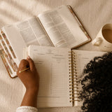 Hands writing in The Anchored Planner beside an open Bible